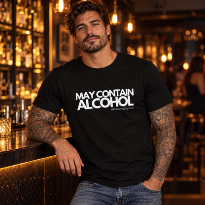 Tattooed man wearing black May Contain Alcohol T-shirt in a warmly lit bar
