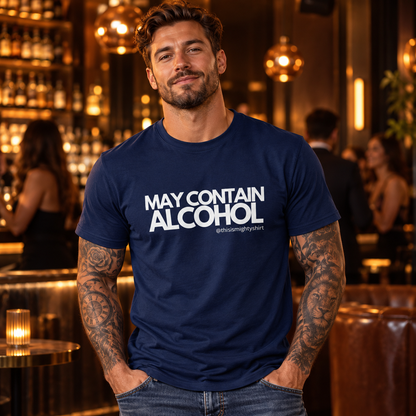 Tattooed man wearing navy May Contain Alcohol T-shirt in a warmly lit bar
