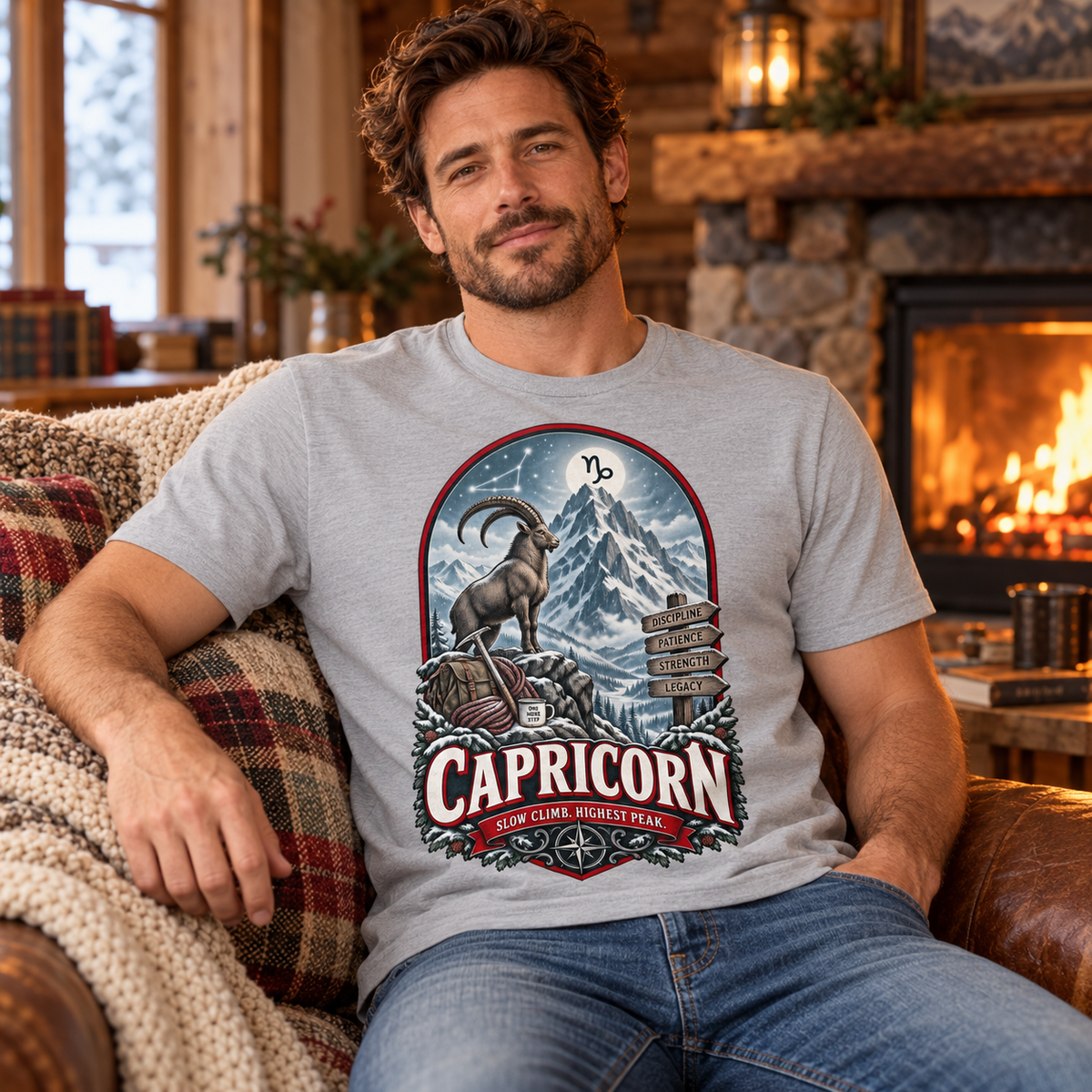 Capricorn Slow Climb Highest Peak Men's T-Shirt in Sports Grey, model seated cosily on a sofa beside a fireplace in a warm cottage