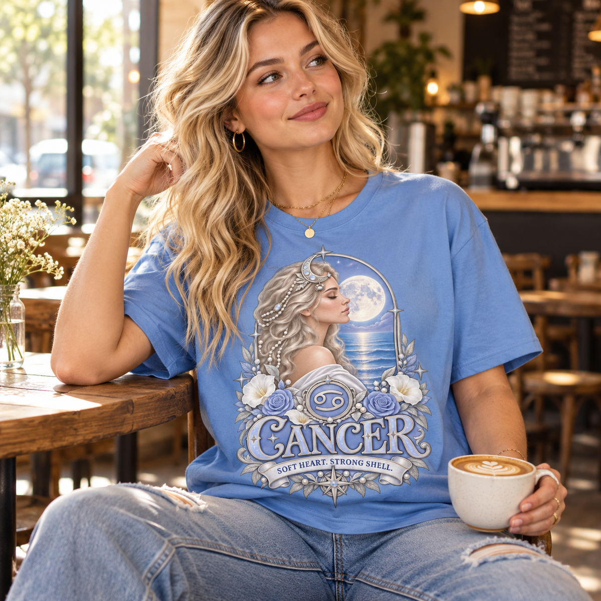 Cancer Soft Heart Strong Shell Women's T-Shirt – Light in Carolina Blue, model inside a stylish warm coffee shop with window light